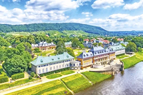 Luftaufnahme des Schlosses Pillnitz an einem sonnigen Tag mit Bergen im Hintergrund.