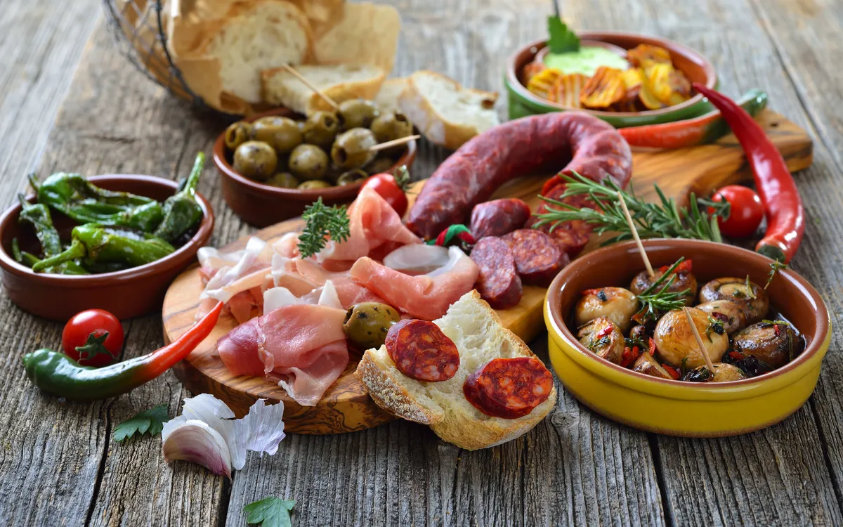 Verschiedene Tapas auf Holztisch mit Schinken, Oliven, Paprika und Brot.