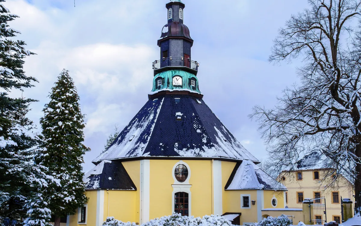 Seiffener Rundkirche im Schnee, umgeben von Bäumen und einem Friedhof im Erzgebirge.