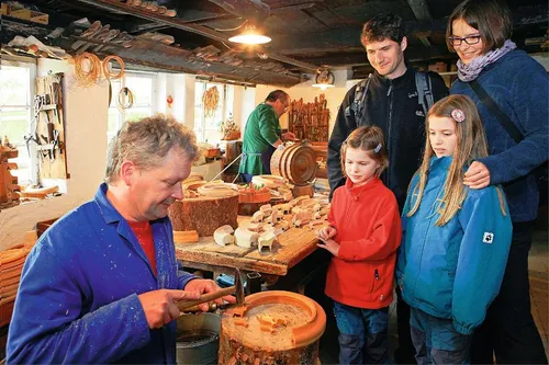 Reifendreher zeigt Touristen in Seiffen Handwerk an der Holzdrehbank.