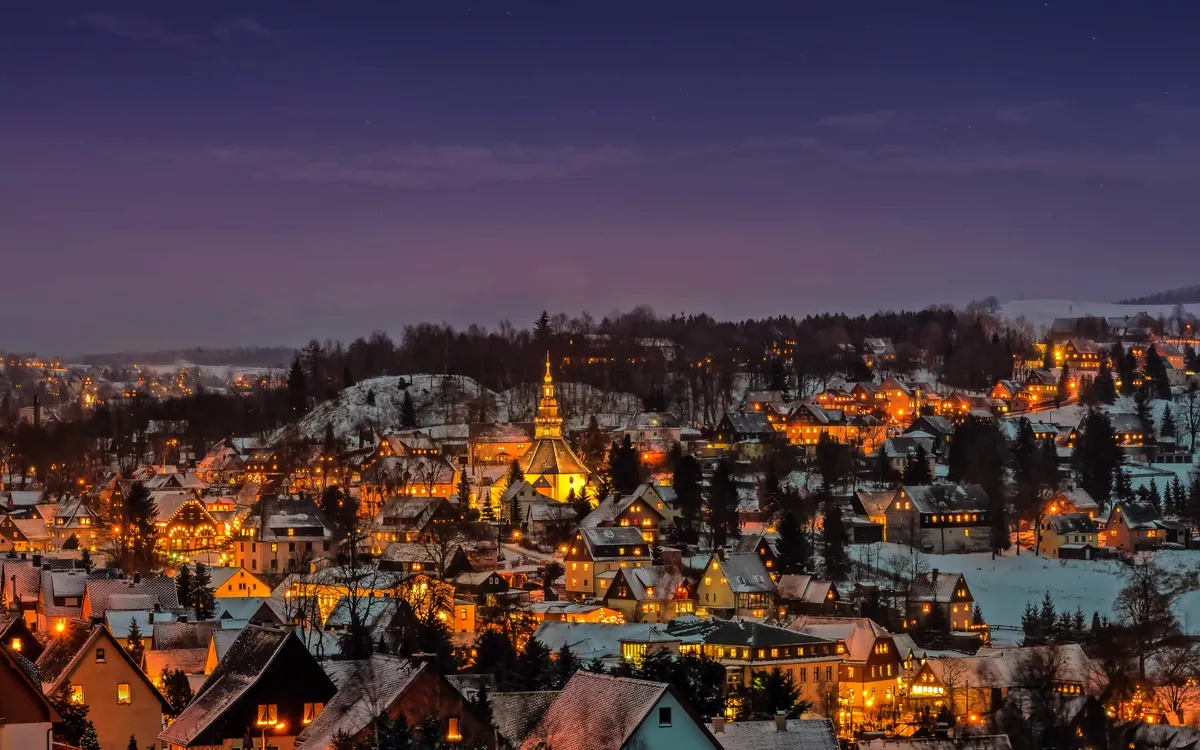 Winterliche Nachtansicht von Seiffen im Erzgebirge mit beleuchteten Häusern im Schnee.