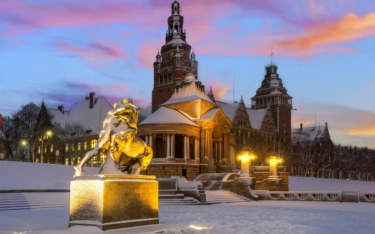 Schneebedeckter Platz mit Reiterstatue und historischer Architektur bei Sonnenuntergang.