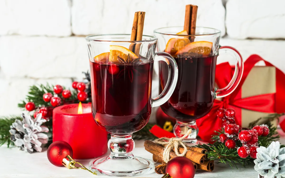 Glühwein im Glasbecher mit Frucht und Gewürzen auf Weiß.