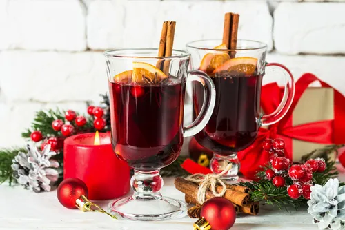 Glühwein im Glasbecher mit Frucht und Gewürzen auf Weiß.