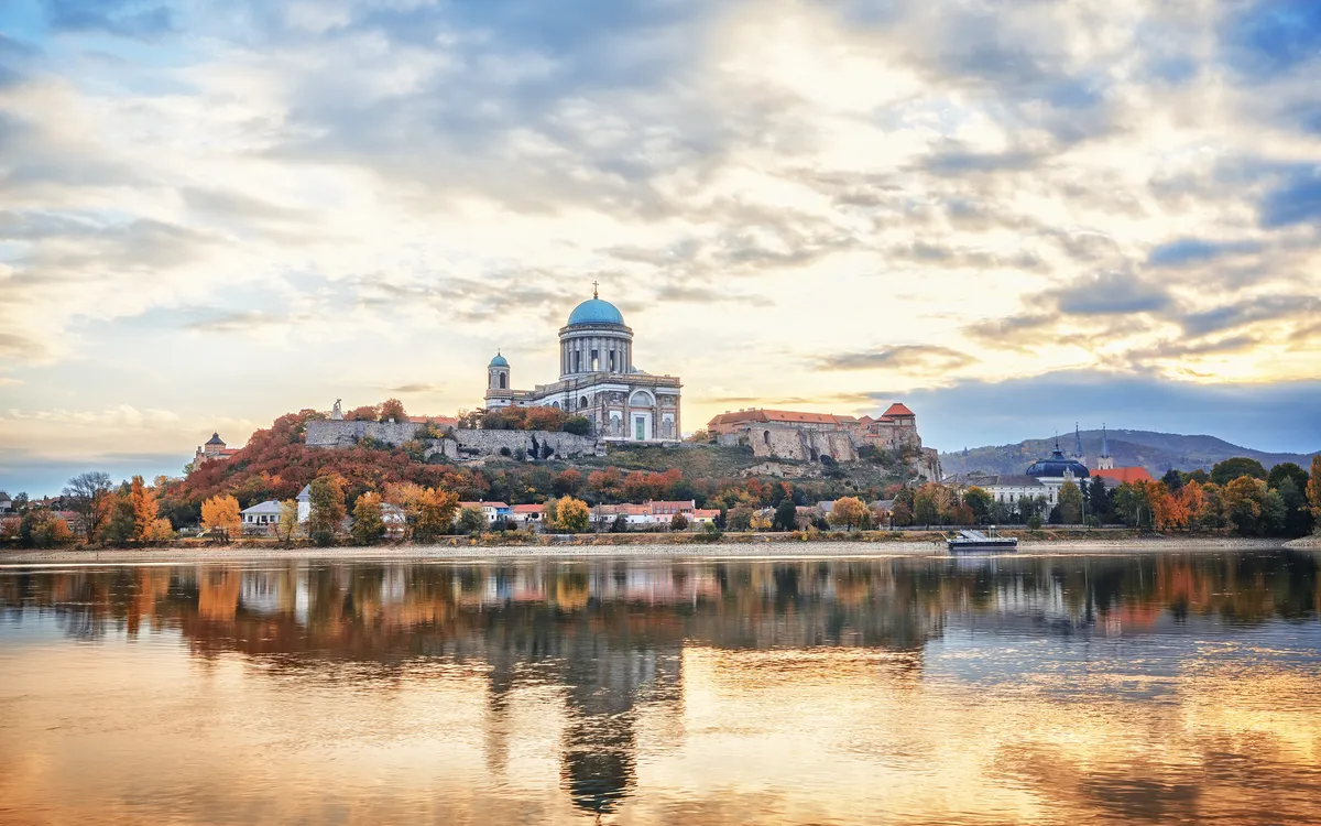Basilika auf Hügel am Ufer eines Flusses bei Sonnenuntergang, Bäume im Herbstlaub.