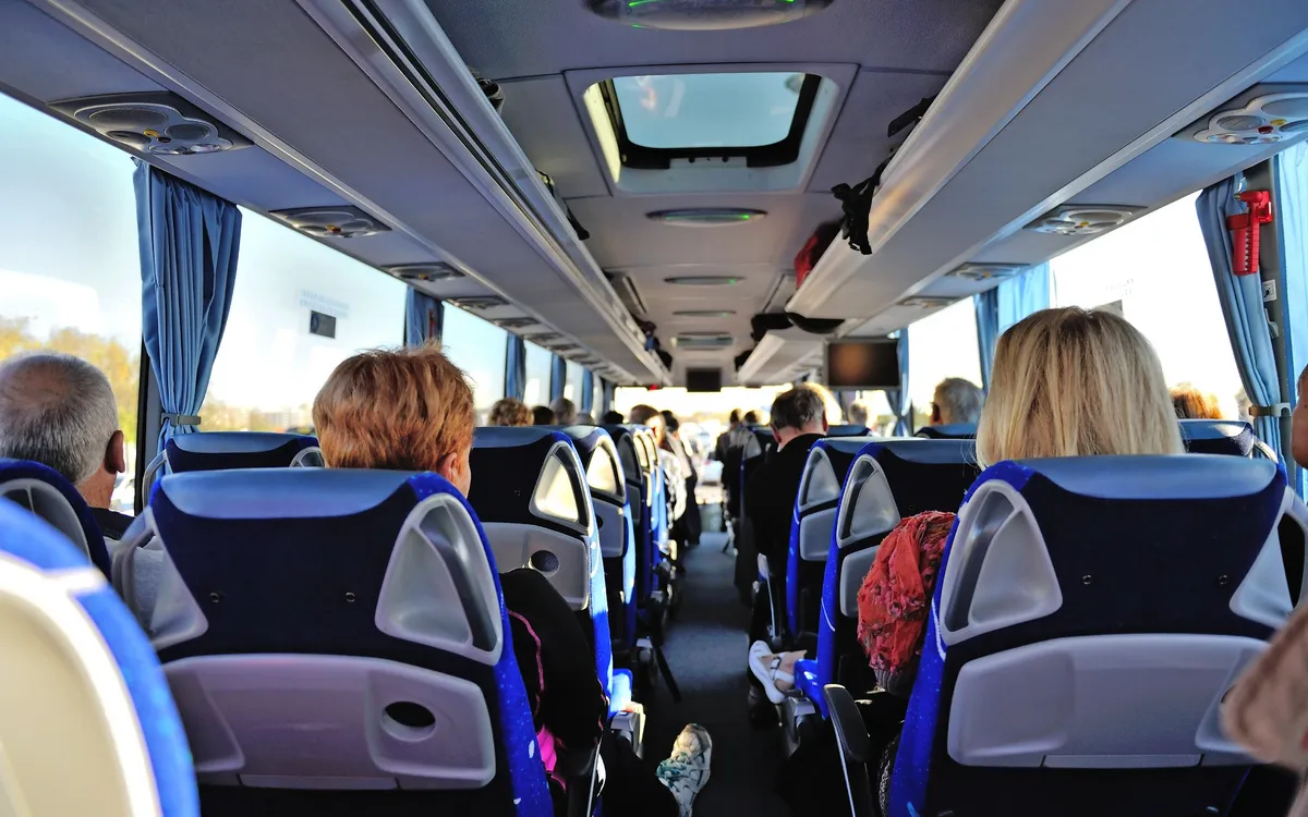 Innenansicht eines fahrenden Reisebusses mit sitzenden Fahrgästen.