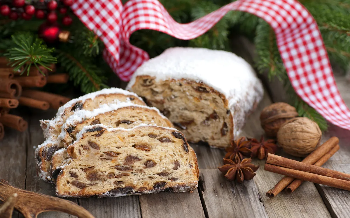 Weihnachtsstollen mit Zimtstangen und Nüssen auf Holztisch.