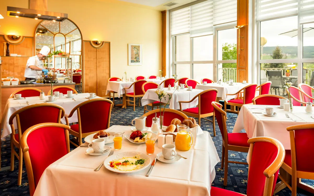 Restaurant mit gedeckten Tischen und Frühstücksbuffet im Hintergrund.
