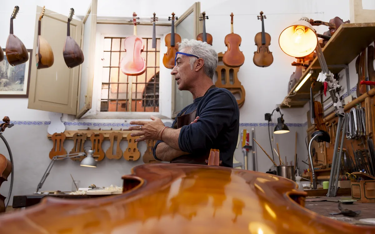Mann arbeitet in einer Werkstatt mit Musikinstrumenten und Geigen an der Wand.