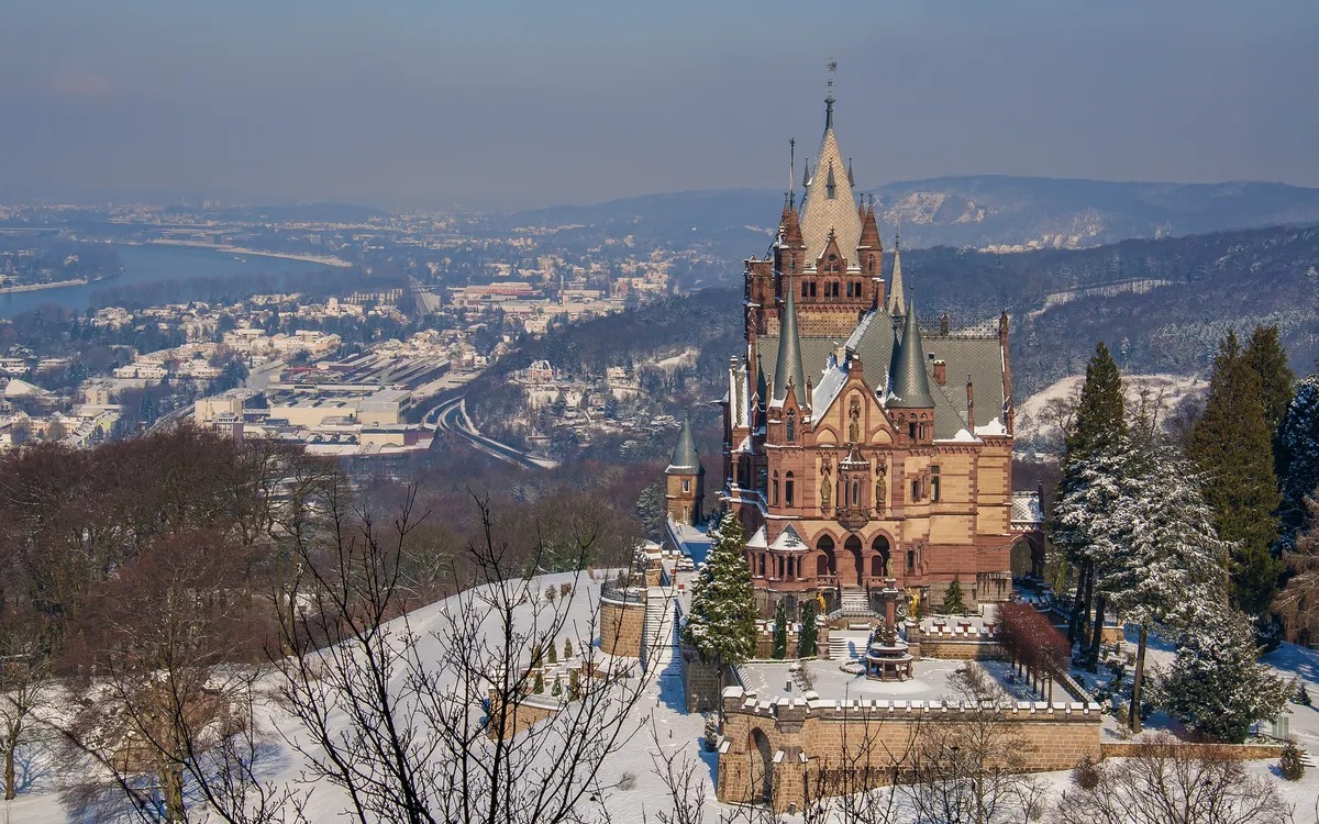 Ein Schloss auf einem Hügel mit Blick auf eine verschneite Landschaft und Stadt im Hintergrund.