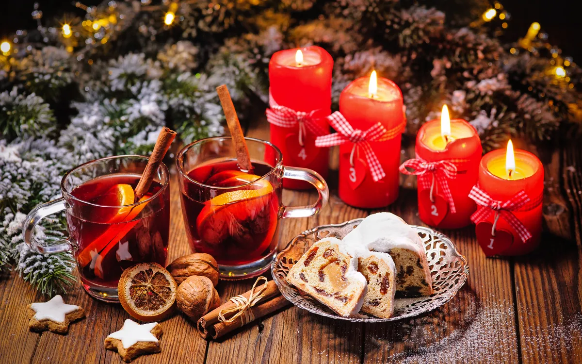 Weihnachtliche Szene mit Glühwein, Stollen und roten Kerzen.