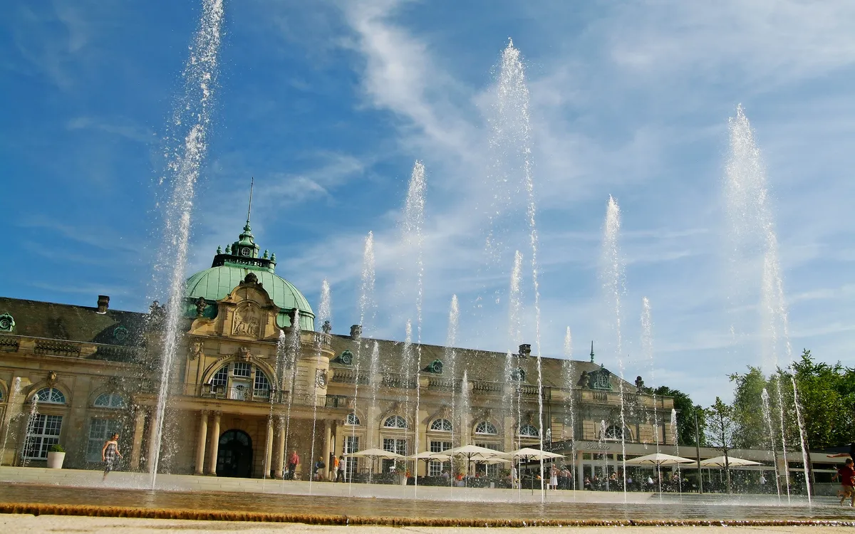 Historisches Gebäude mit Springbrunnen im Vordergrund.