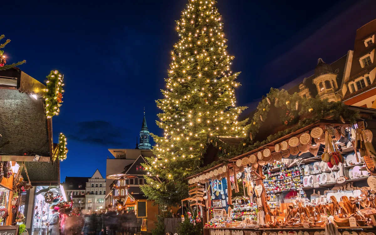 Weihnachtsmarkt mit beleuchtetem Tannenbaum und Verkaufsständen am Abend.