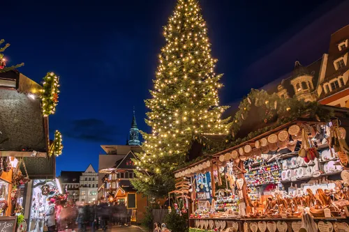 Weihnachtsmarkt mit beleuchtetem Tannenbaum und Verkaufsständen am Abend.