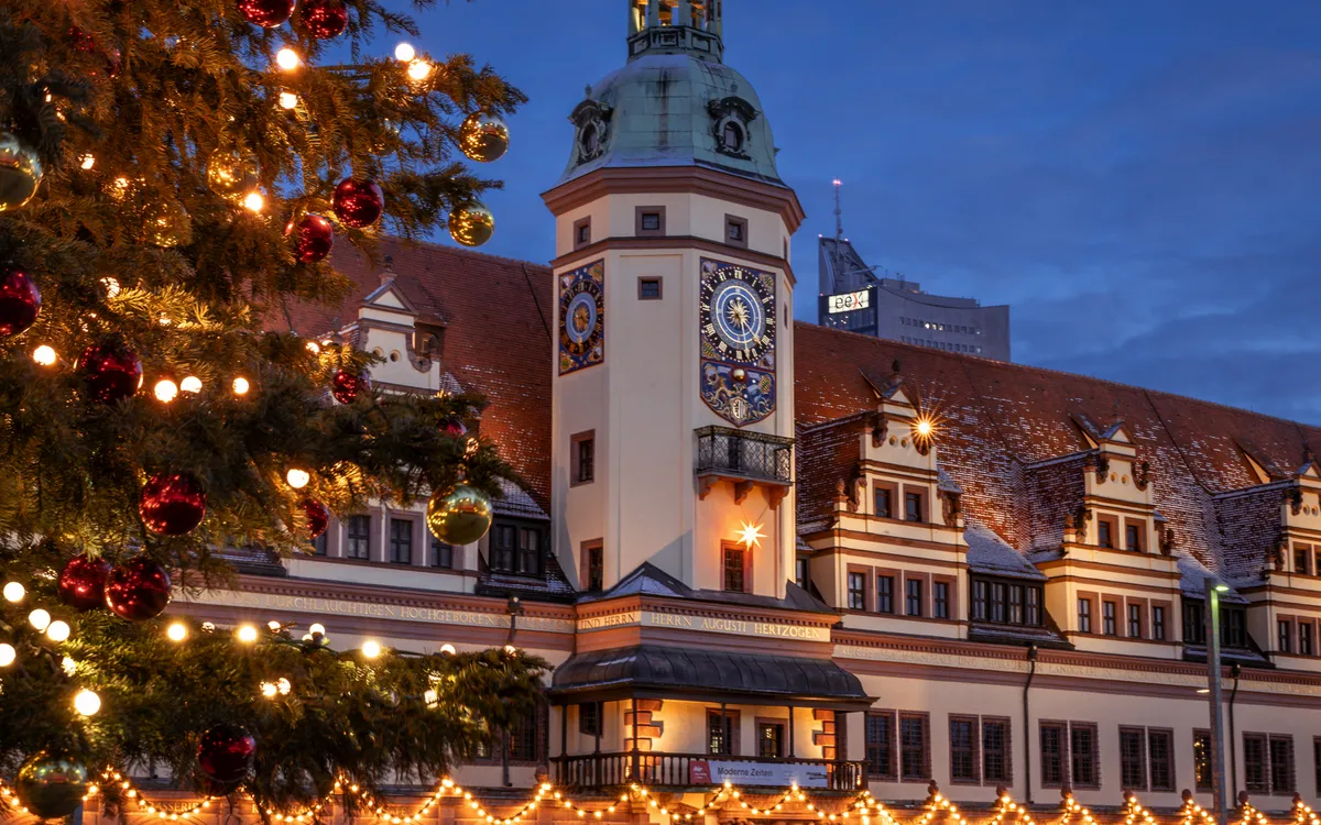 Weihnachtlich beleuchtetes historisches Gebäude bei Dämmerung, neben einem geschmückten Baum.