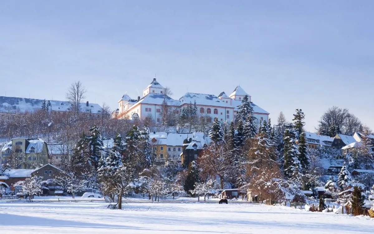 Schloss bei winterlicher Schneelandschaft und blauem Himmel.