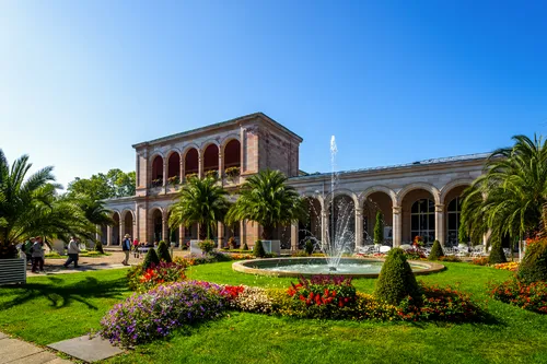 Historisches Gebäude mit Arkaden, Brunnen und Garten.