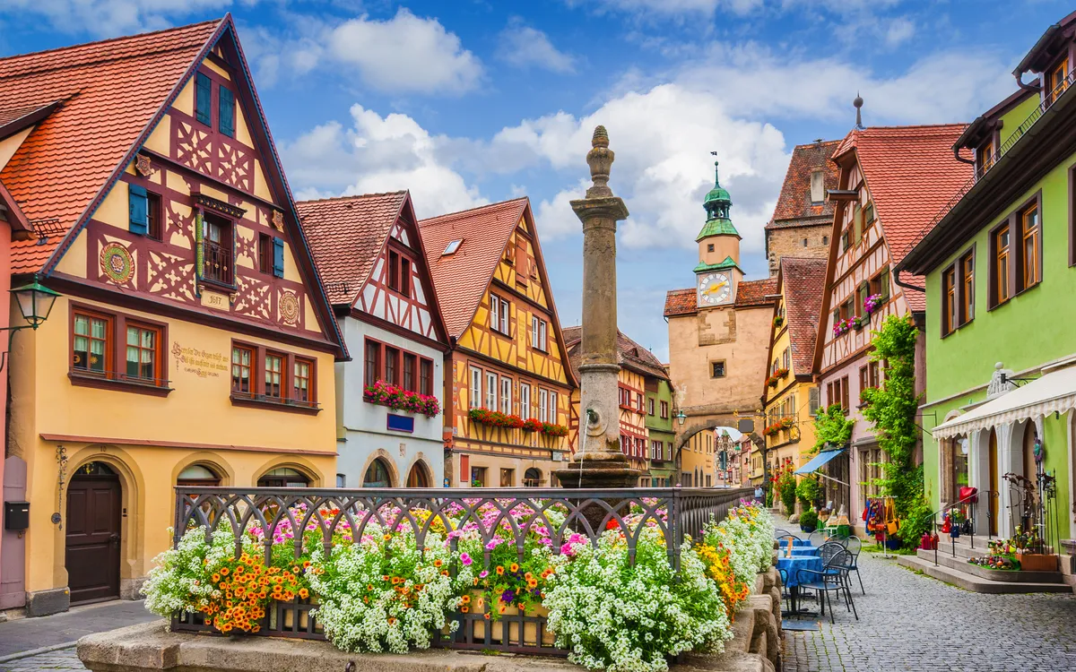 Fachwerkhäuser mit Blumen und Brunnen auf Kopfsteinpflasterstraße.