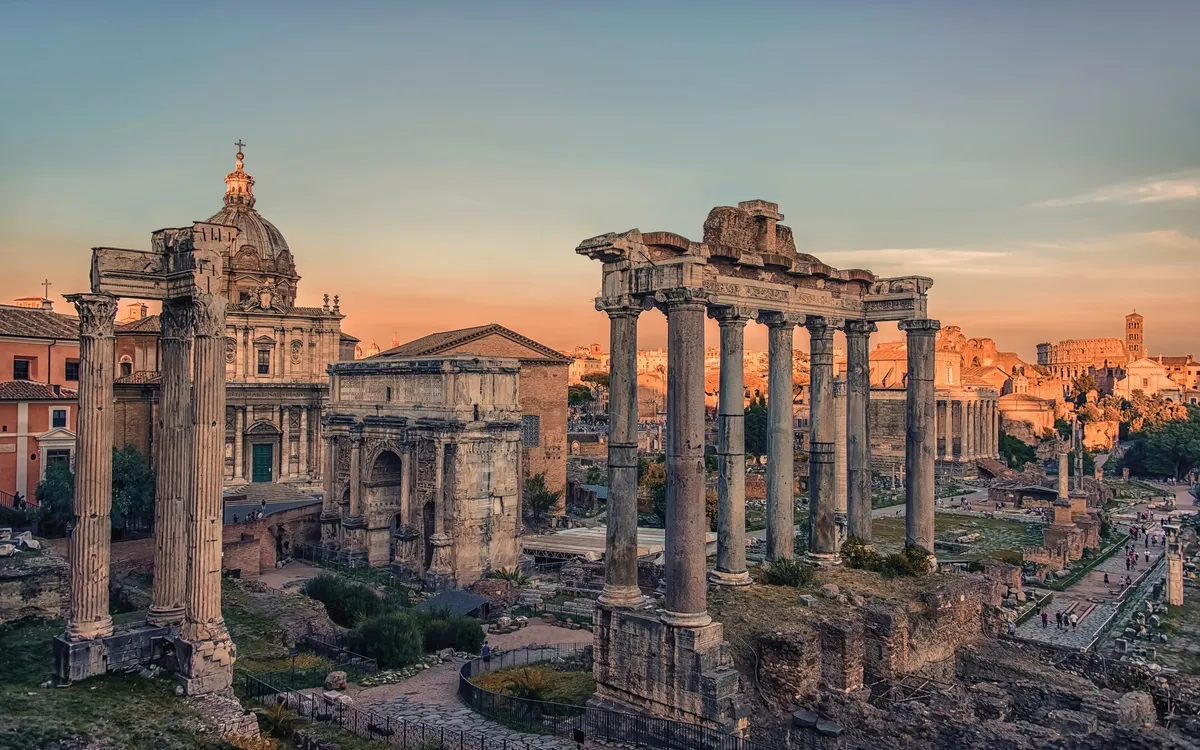 Forum Romanum in Rom bei Sonnenuntergang mit antiken Ruinen und Säulen im Vordergrund.