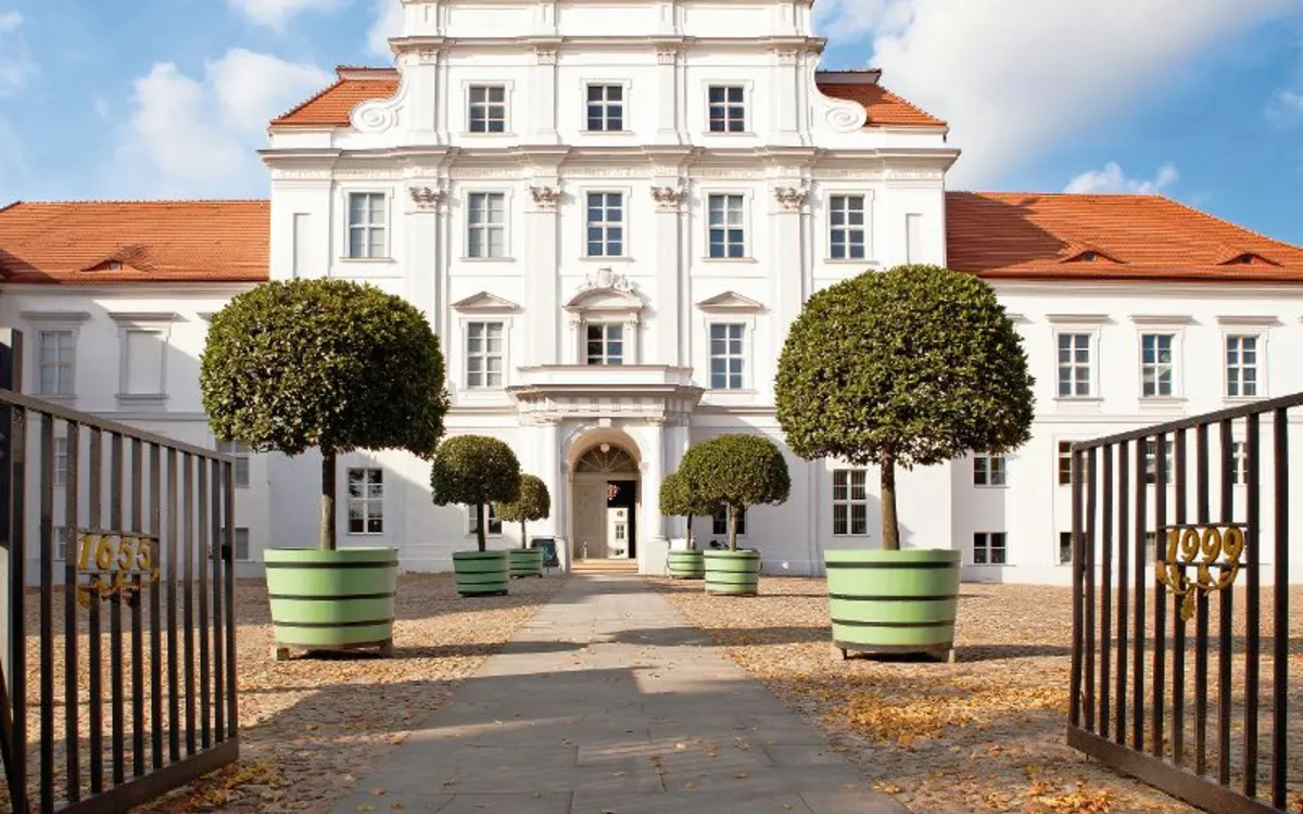 Barocke Fassade von Schloss Oranienburg mit Einfahrt und Tor im Vordergrund.