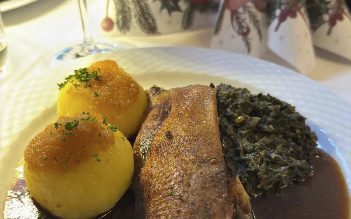 Gedeckter Tisch mit Entenbraten, Klößen, Rotkraut und Rotweinglas.