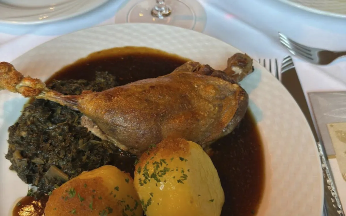 Gedeckter Tisch mit Gänsekeule, Kartoffeln und Rotwein.