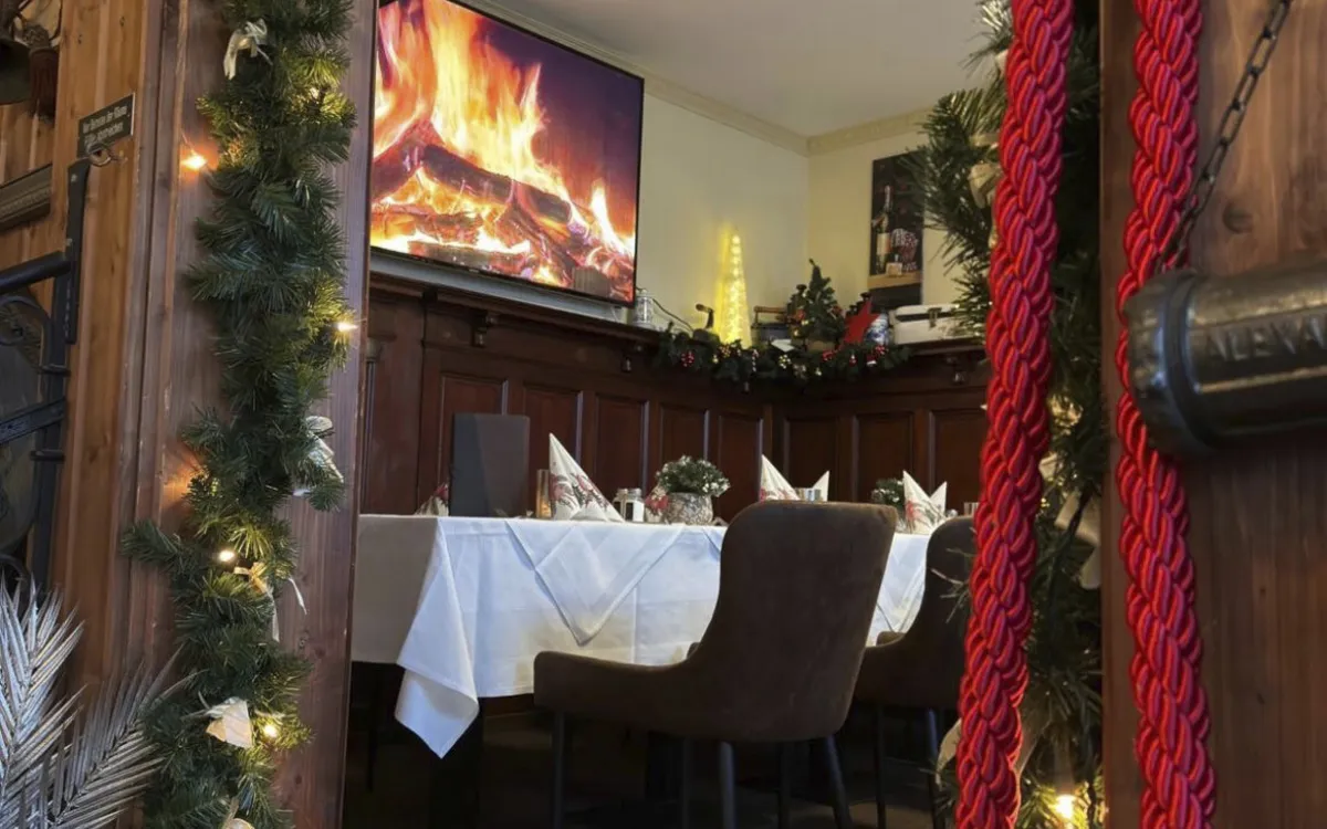 Festlich dekoriertes Restaurant mit Weihnachtsschmuck und Kaminbild auf Bildschirm.