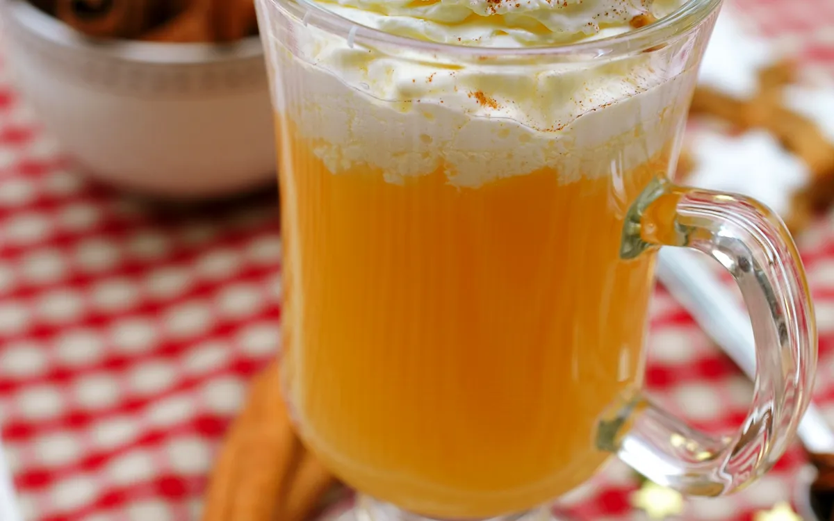 Heißer Eierpunsch mit Sahne und Zimtstangen auf Weihnachtstisch mit Keksen.