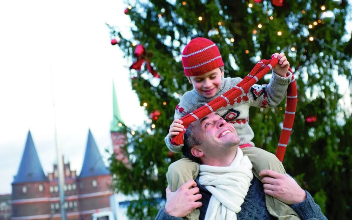Vater mit Sohn auf den Schultern vor geschmücktem Weihnachtsbaum in Lübeck.