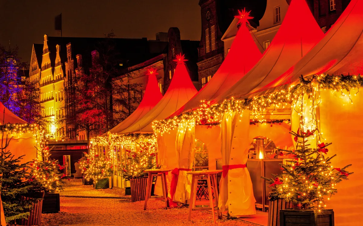 Weihnachtsmarkt in Lübeck mit Lichterketten bei Nacht entlang des Flusses.
