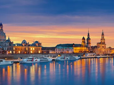 Stadtpanorama von Dresden bei Sonnenuntergang mit Elbe und beleuchteten Gebäuden.