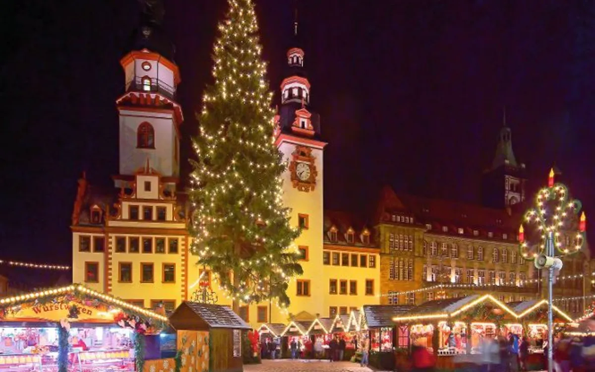 Beleuchteter Weihnachtsmarkt mit Tannenbaum und historischen Gebäuden bei Nacht.