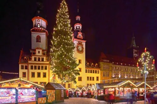 Beleuchteter Weihnachtsmarkt mit Tannenbaum und historischen Gebäuden bei Nacht.