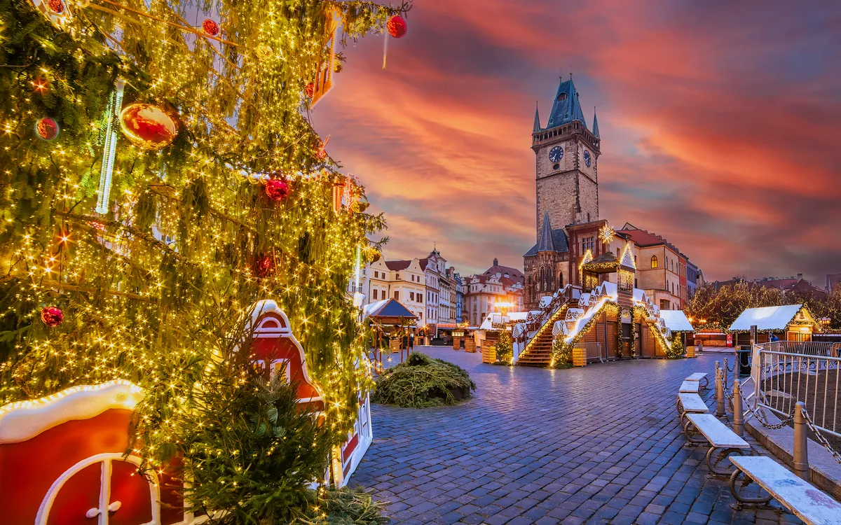 Weihnachtsmarkt bei Sonnenuntergang mit Weihnachtsbaum und Uhrenturm im Hintergrund