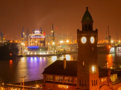 Nachtaufnahme der beleuchteten St. Pauli Landungsbrücken mit Kränen in Hamburg.