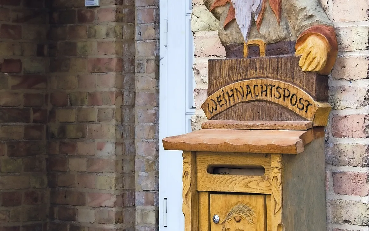 Postkasten mit Weihnachtsmannfigur an Backsteinwand.