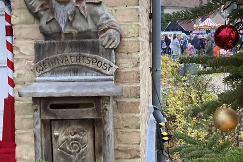 Weihnachtspostkasten mit Elfenfigur neben geschmücktem Tannenbaum.
