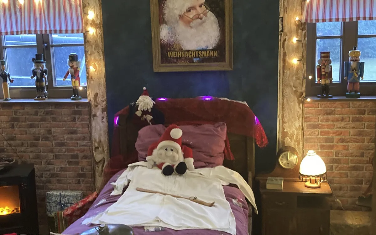 Weihnachtlich dekoriertes Schlafzimmer mit Santa-Porträt und Lichterketten.
