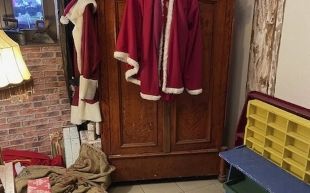 Rotes Weihnachtsmannkostüm hängt an einem Schrank, umgeben von Geschenken und Dekoration.