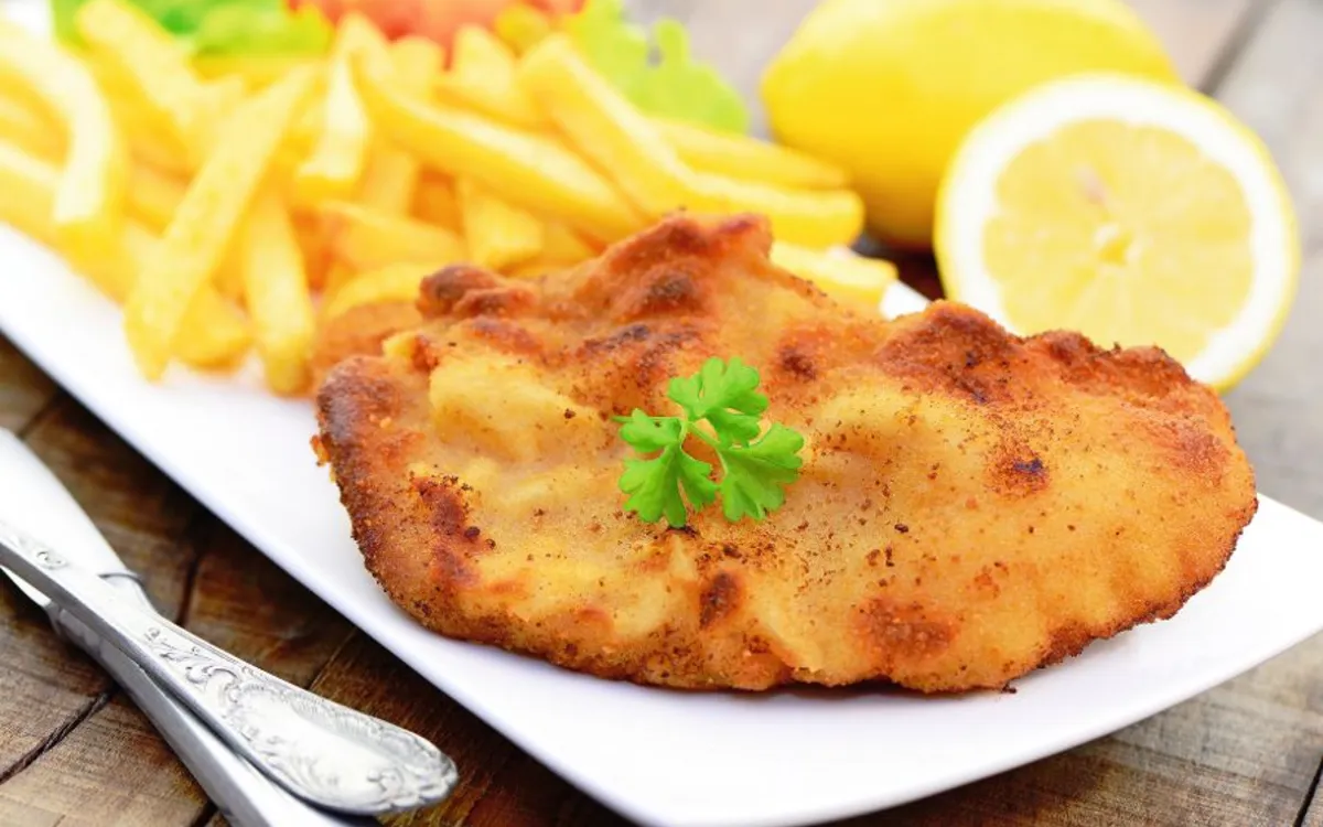 Schnitzel auf Teller mit Pommes, Zitrone und Besteck.