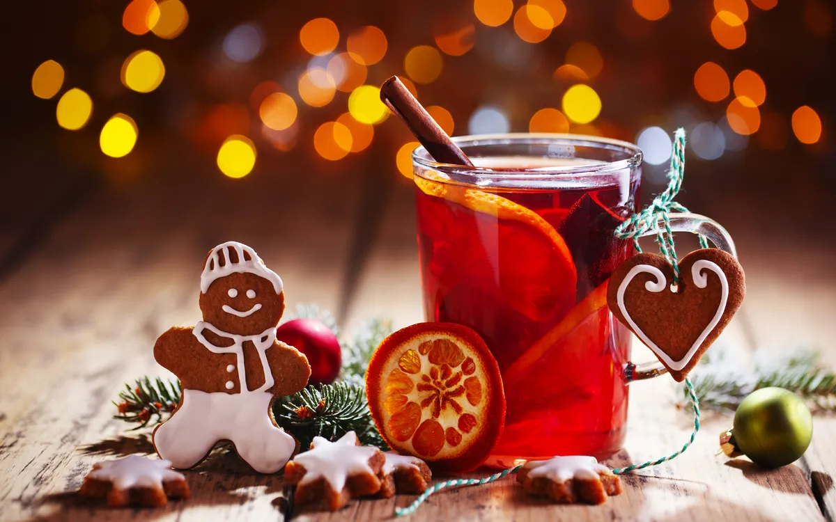 Lebkuchen und Heißgetränk mit Orangenscheiben auf einem weihnachtlich dekorierten Tisch.
