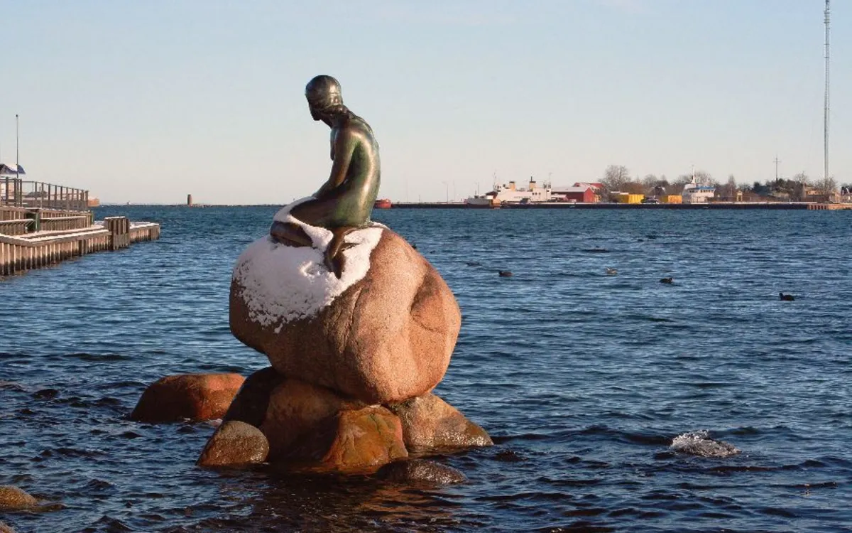 Statue der Kleinen Meerjungfrau auf einem Felsen im verschneiten Kopenhagen am Meer.
