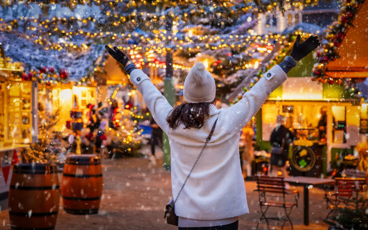 Frau genießt Kopenhagens Weihnachtsmarkt im Winter bei festlicher Beleuchtung.