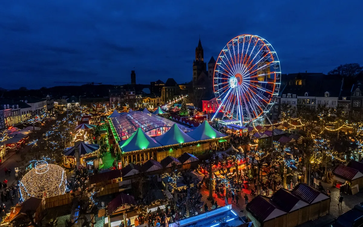 Blick auf bunten Weihnachtsmarkt mit Riesenrad bei Nacht in Maastricht.