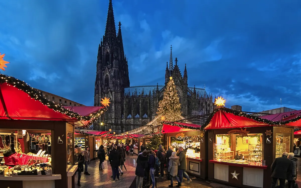 Weihnachtsmarkt mit Kölner Dom im Hintergrund bei Dämmerung.