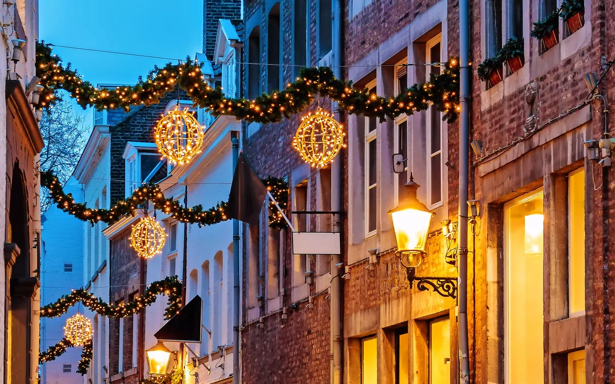 Gepflasterte Gasse mit Weihnachtsbeleuchtung in der Dämmerung.