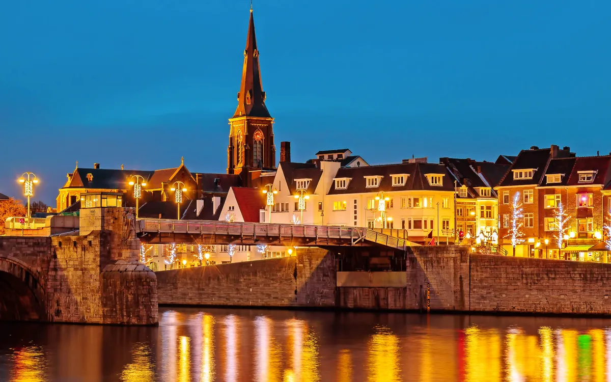 Abendansicht einer Stadt mit Kirche, beleuchteten Gebäuden und Fluss.