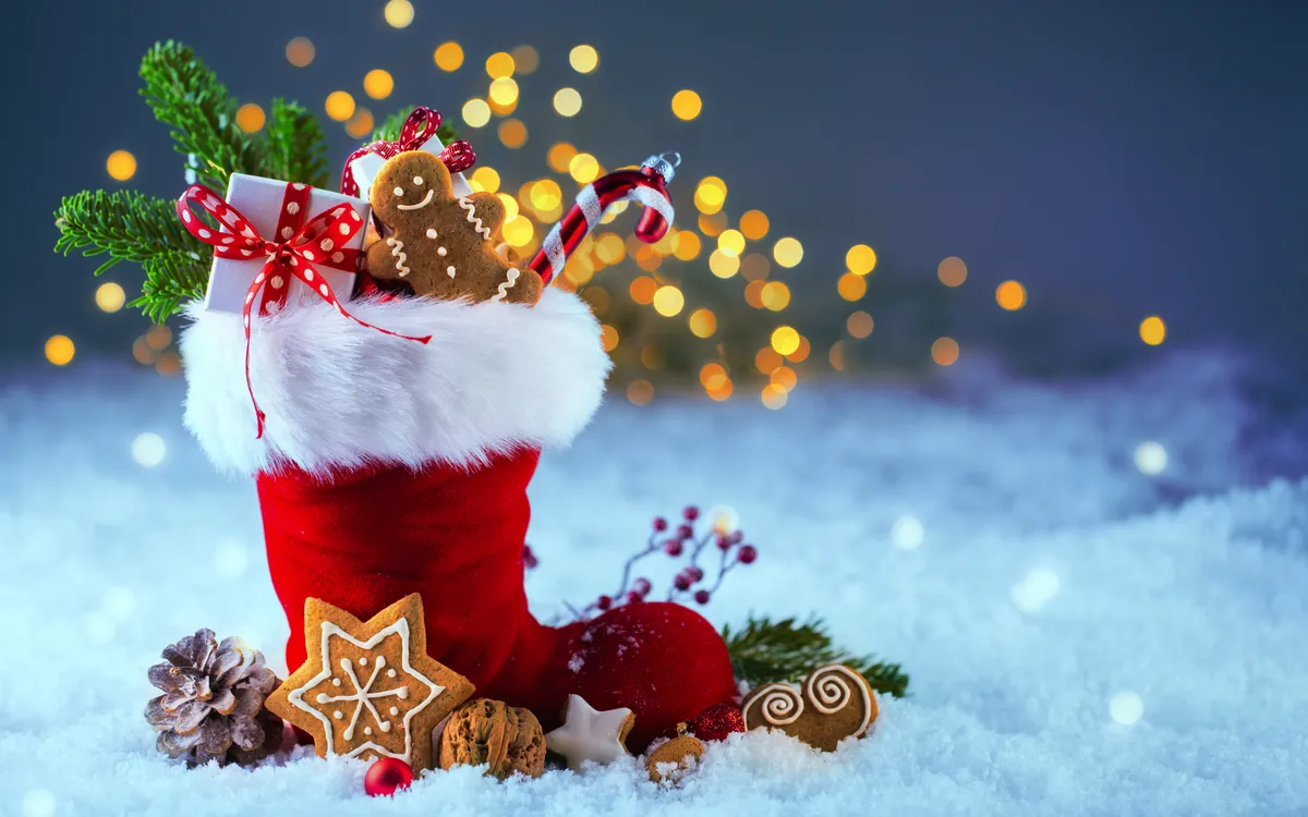 Nikolausstiefel im Schnee mit Lebkuchen und Geschenken vor bokehbeleuchtetem Hintergrund