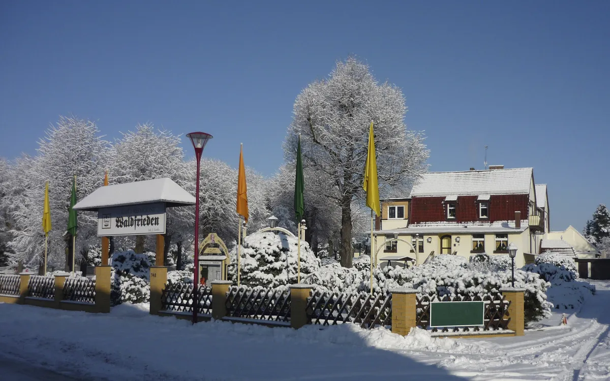 Winterliche Szene mit schneebedecktem Gebäude und Bäumen im Hintergrund.