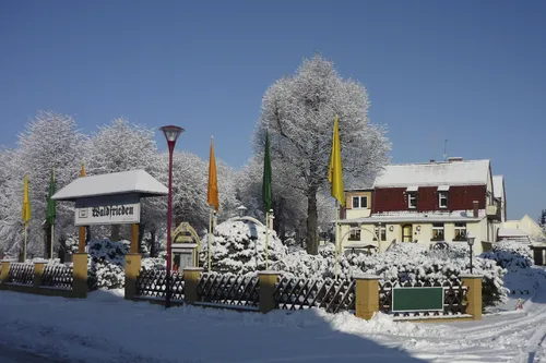 Winterliche Szene mit schneebedecktem Gebäude und Bäumen im Hintergrund.